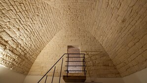 A stone vaulted ceiling with a wooden staircase leading to a small window. - Trulli in corte (Alberobello)