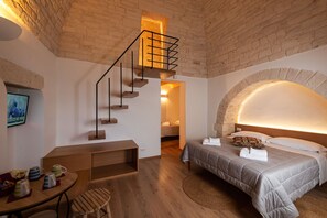 A modern bedroom with a wooden staircase, a bed with a headboard, a desk, and a TV on the wall.