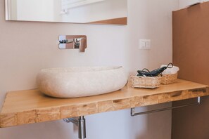 A bathroom with a large, round, beige ceramic sink, a wooden countertop, a mirror, and a small basket with a towel.