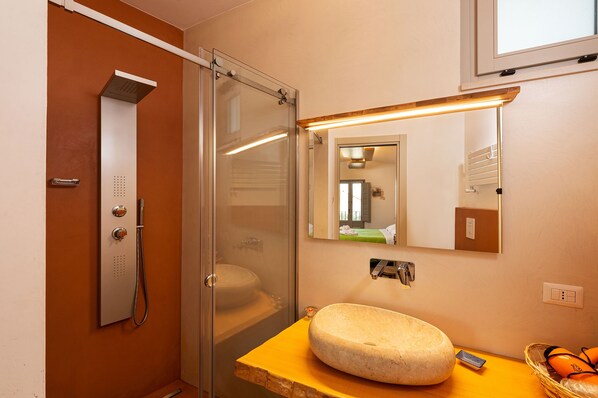 Un baño con cabina de ducha de vidrio, lavabo con encimera de mármol, espejo y ventana sobre el espejo.