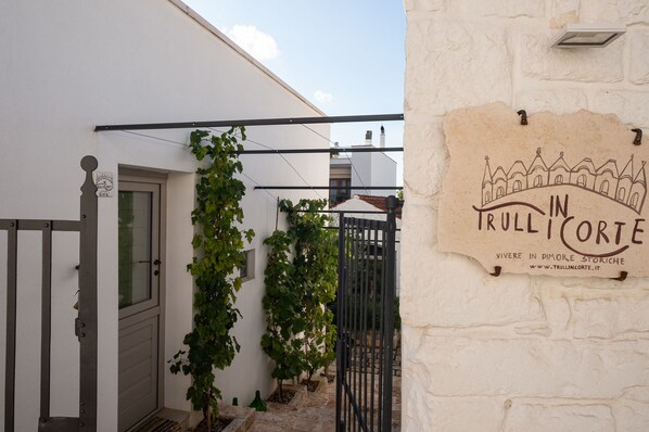 A white building with a sign reading "In Trull Corte" and a metal gate. - Trulli in corte (Alberobello)
