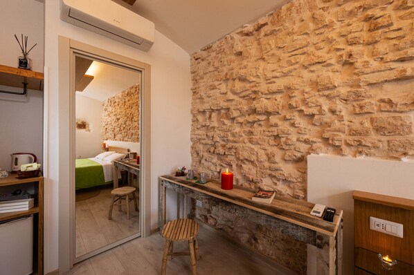 A room with a stone wall, a wooden desk, a mirror, a bed with a green bedspread, and a small stool. - Trulli in corte (Alberobello)