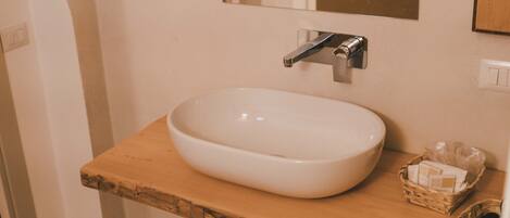 A bathroom with a white sink, wooden countertop, and a mirror above it.