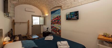 A bedroom with a brick ceiling, a bed with blue bedding, a painting on the wall, and a small table with towels.
