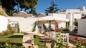 A courtyard with a stone fountain, white outdoor furniture, and a covered seating area. - Trulli in corte (Alberobello)