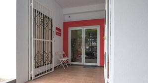 A room with a tiled floor, a white door with a metal gate, and a red wall. - RedDoorz near ITC Mangga Dua (Jakarta)