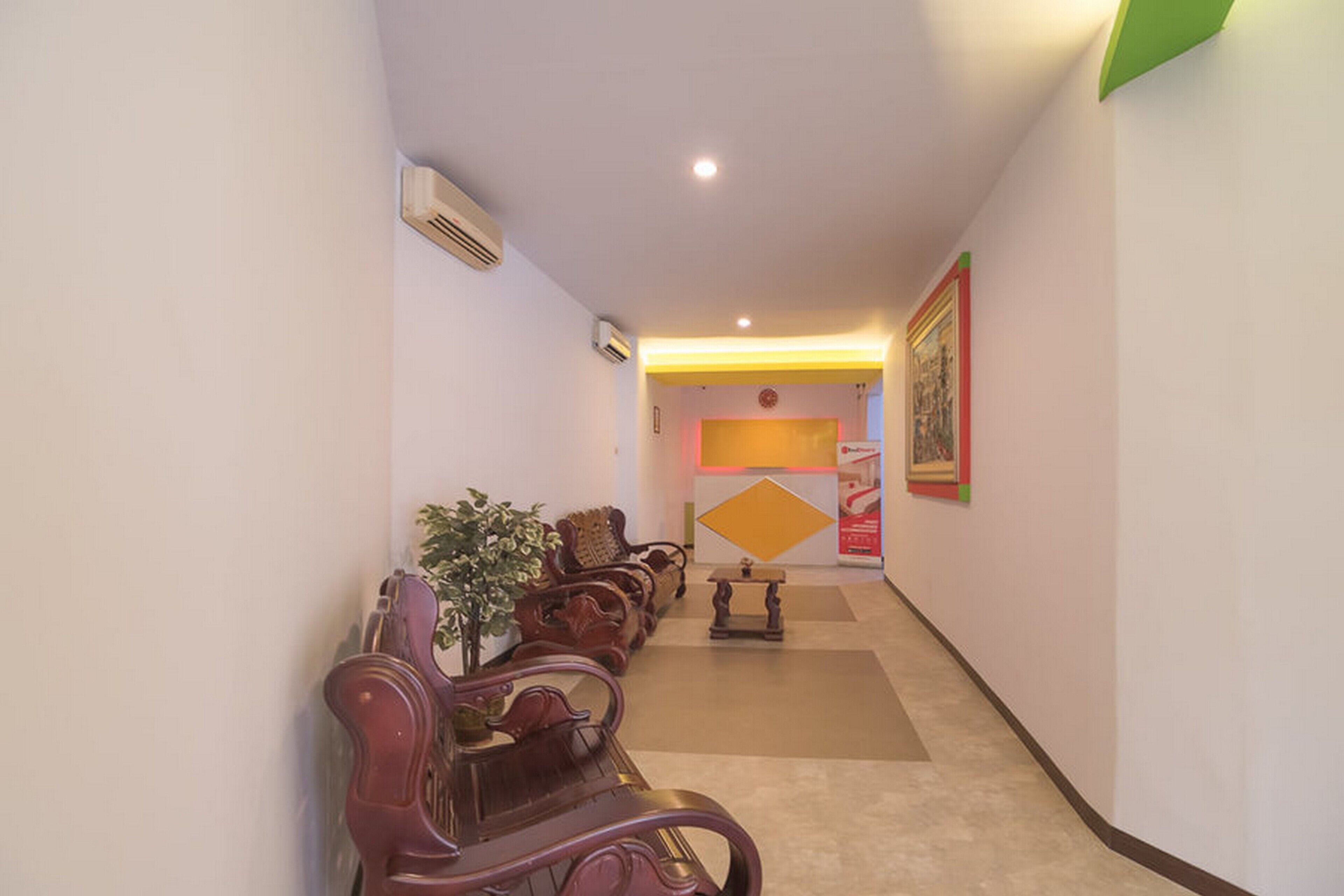 A hallway with wooden benches, a potted plant, and a reception desk with a sign.