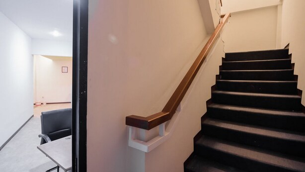 A modern staircase with wooden handrails and black steps, leading to a room with a white wall and a door. - RedDoorz near ITC Mangga Dua (Jakarta)