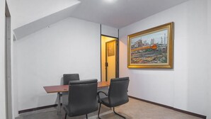 A conference room with a wooden table, two black chairs, and a framed cityscape painting on the wall. - RedDoorz near ITC Mangga Dua (Jakarta)