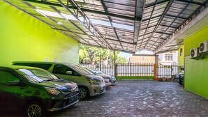A covered parking area with several cars parked, a green wall, and a metal roof structure. - RedDoorz near Kejaksan Station Cirebon 2 (North Cirebon)