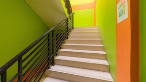 A staircase with beige steps and a black railing, surrounded by walls painted in green and orange. - RedDoorz near Kejaksan Station Cirebon 2 (North Cirebon)