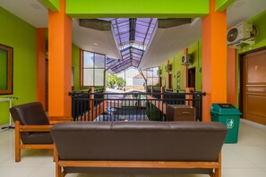 A hotel lobby with a central seating area, a glass ceiling, and a view of the street outside. - RedDoorz near Kejaksan Station Cirebon 2 (North Cirebon)