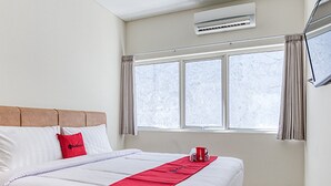 Une chambre d’hôtel avec un grand lit, un plaid rouge et une fenêtre avec des rideaux.