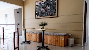 A reception area with a wooden bench, a small table with a plant, and a trash bin. - RedDoorz near Kebun Raya Bogor 2 (Bogor)