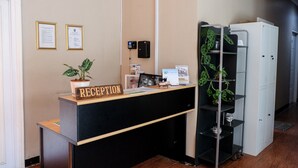 A reception desk with a sign reading "RECEPTION," a potted plant, a small shelf with a book, and a wall-mounted device. - RedDoorz near Kebun Raya Bogor 2 (Bogor)