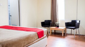 A hotel room with a bed, two chairs, a small table with a plant, and a window with curtains. - RedDoorz near Kebun Raya Bogor 2 (Bogor)