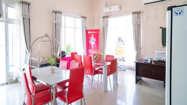 A hotel room with a dining area featuring red chairs and a glass table, a desk with a computer, and a large window with curtains. - RedDoorz @ Jalan Pendidikan Mataram (Mataram)