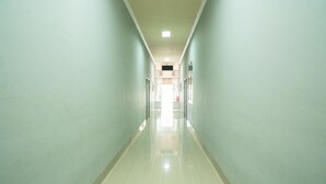A long, narrow hallway with light-colored walls and a shiny floor, leading to a door at the end. - RedDoorz @ Jalan Pendidikan Mataram (Mataram)