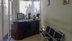 A reception desk with a computer, a plant, and a framed certificate. There are two black chairs to the right. - RedDoorz Hostel @ Manado Green Hostel (Manado)