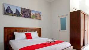 Habitación de hotel con cama de madera, ropa de cama blanca, almohada decorativa roja y cubrecama rojo. Se observa un armario de madera y una puerta con panel azul.