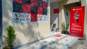 Un cartel de RedDoorz que anuncia alojamiento económico, una pared con diseño, plantas en macetas y una silla frente a un edificio.