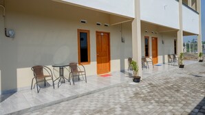 Un espacio exterior techado con varias puertas y ventanas, mobiliario exterior con sillas y mesas, y plantas en macetas.