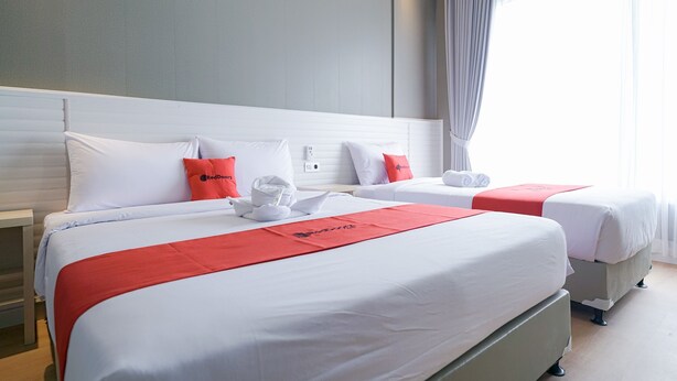 Une chambre d’hôtel avec deux lits, du linge de lit blanc, des touches de couleur rouge et une vue sur l’extérieur.