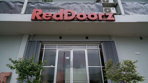 Un bâtiment RedDoorz doté d’une grande entrée en verre, de plantes en pot et d’un auvent gris.