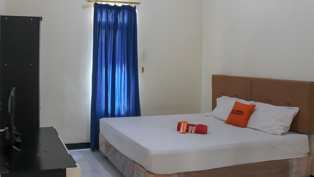 A bedroom with a bed, pillows, a TV on a stand, and a curtain. - KoolKost Syariah near Universitas Ahmad Dahlan Kampus 1 (Yogyakarta)