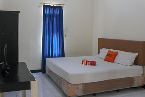 A bedroom with a bed, pillows, a TV on a stand, and a curtain. - KoolKost Syariah near Universitas Ahmad Dahlan Kampus 1 (Yogyakarta)