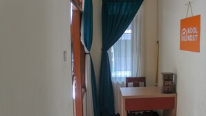 A room with a wooden table, a chair, a small cabinet, teal curtains, and a sign reading "KOOL KOST". - KoolKost Syariah near Universitas Ahmad Dahlan Kampus 1 (Yogyakarta)