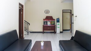 A waiting area with two black sofas, a wooden table with a small bowl, a fish tank, and a water dispenser. - KoolKost Syariah near Universitas Ahmad Dahlan Kampus 1 (Yogyakarta)
