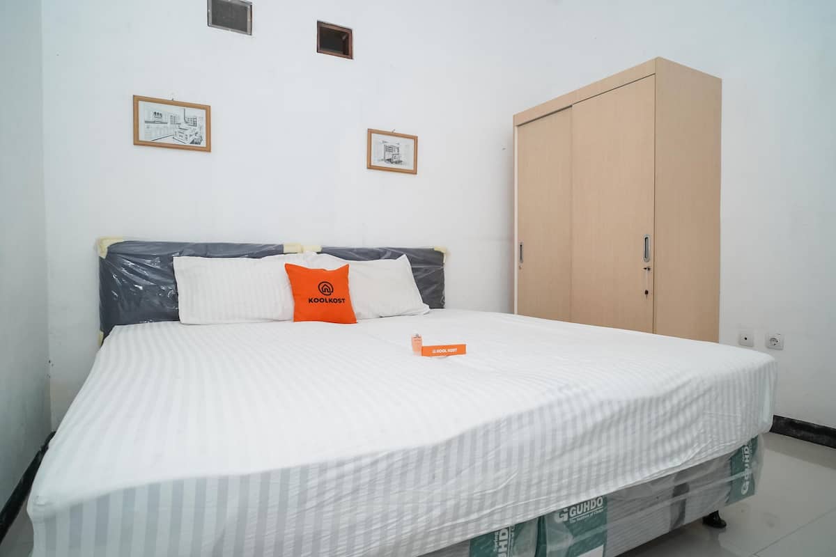 A bedroom with a bed, two framed pictures on the wall, a wardrobe, and a small window.