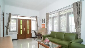 A living room with a green sofa, a wooden coffee table, a desk with a chair, and a door with glass panels. - KoolKost @ Batutulis Bogor (Bogor)
