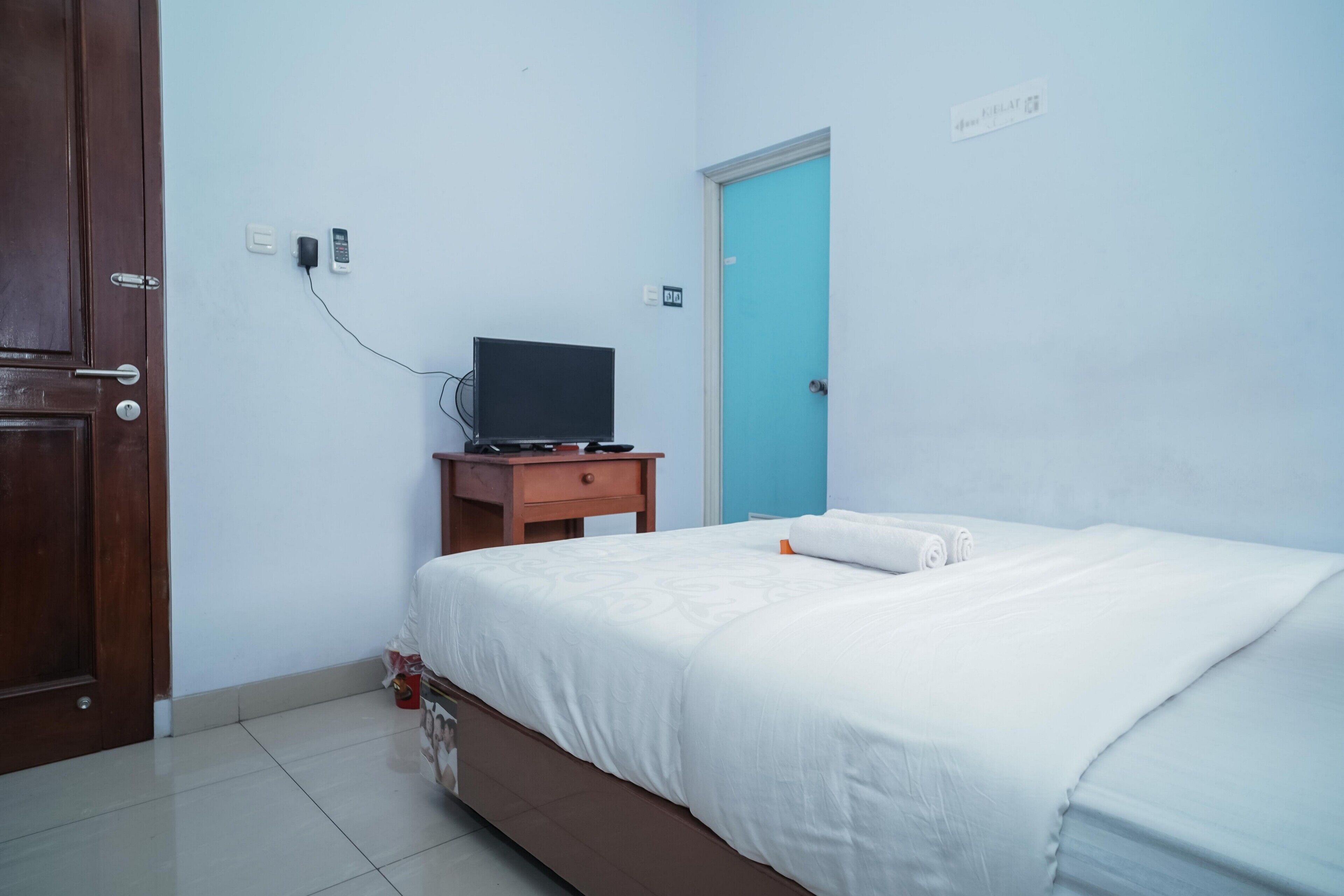 A bedroom with a bed, a wooden nightstand, a television, and a blue door.