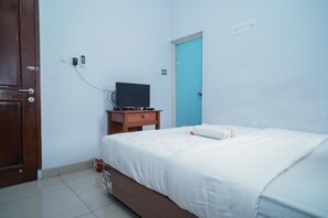 A bedroom with a bed, a wooden nightstand, a television, and a blue door. - KoolKost Syariah @ Duri Kosambi (Jakarta)