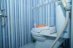 A bathroom with striped blue and white tiles, a toilet, a handheld showerhead, and a toilet paper dispenser labeled "KOOL KOST". - KoolKost Syariah @ Duri Kosambi (Jakarta)