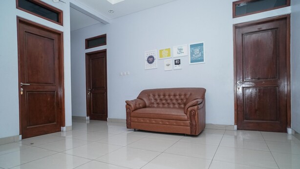 A spacious room with a large brown leather sofa, wooden doors, and a tiled floor. - KoolKost Syariah @ Duri Kosambi (Jakarta)