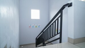A staircase with a black handrail, a small window, and three safety signs on the wall. - KoolKost Syariah @ Duri Kosambi (Jakarta)