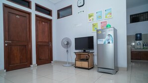 A room with two wooden doors, a television on a wooden stand, a refrigerator, a fan, and a water dispenser. - KoolKost Syariah @ Duri Kosambi (Jakarta)