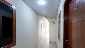 Un couloir avec un sol carrelé, une porte en bois portant une plaque numérotée et un luminaire au plafond.