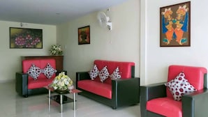 Une pièce comprenant trois canapés rouges à armature noire, chacun agrémenté d’un coussin blanc à pois rouges. Une petite table avec un vase de fleurs est placée au centre.