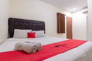 A neatly made bed with a red blanket, a white pillow, and a red pillow with "Red Doors" text.