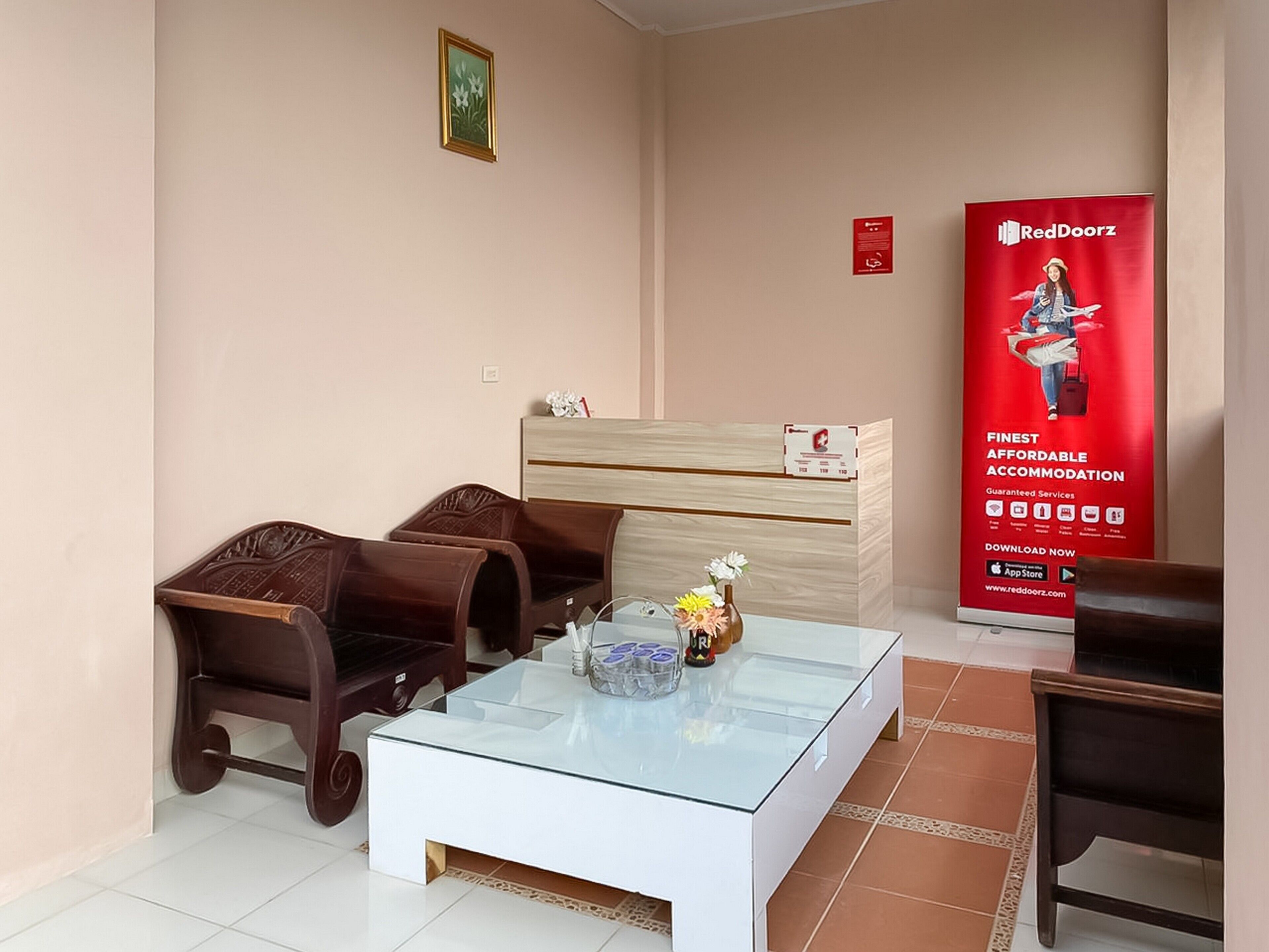 A hotel room with a glass-top coffee table, wooden chairs, a wooden dresser, and a RedDoorz advertisement.