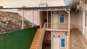 Ein zweistöckiges Gebäude mit einem überdachten Balkon, einem Schild für 'Wika wh' und einer Treppe, die zu der oberen Etage führt.