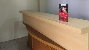A reception desk with a wooden counter and a sign advertising RedDoorz booking apps. - RedDoorz near Institut Kesehatan Helvetia (Medan)