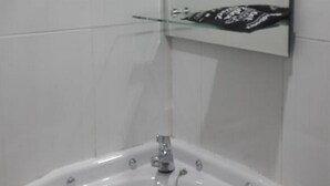Un baño con un lavamanos blanco, un estante de vidrio encima y un espejo que refleja parte de la habitación.
