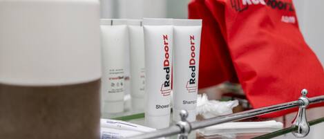 Een badkamerplank met Red Doorz douchegel, shampoo en een rode handdoek.