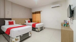 A hotel room with two beds, a TV, an air conditioner, and a small desk with toiletries. - RedDoorz Plus @ Cemara Asri Medan (Medan)