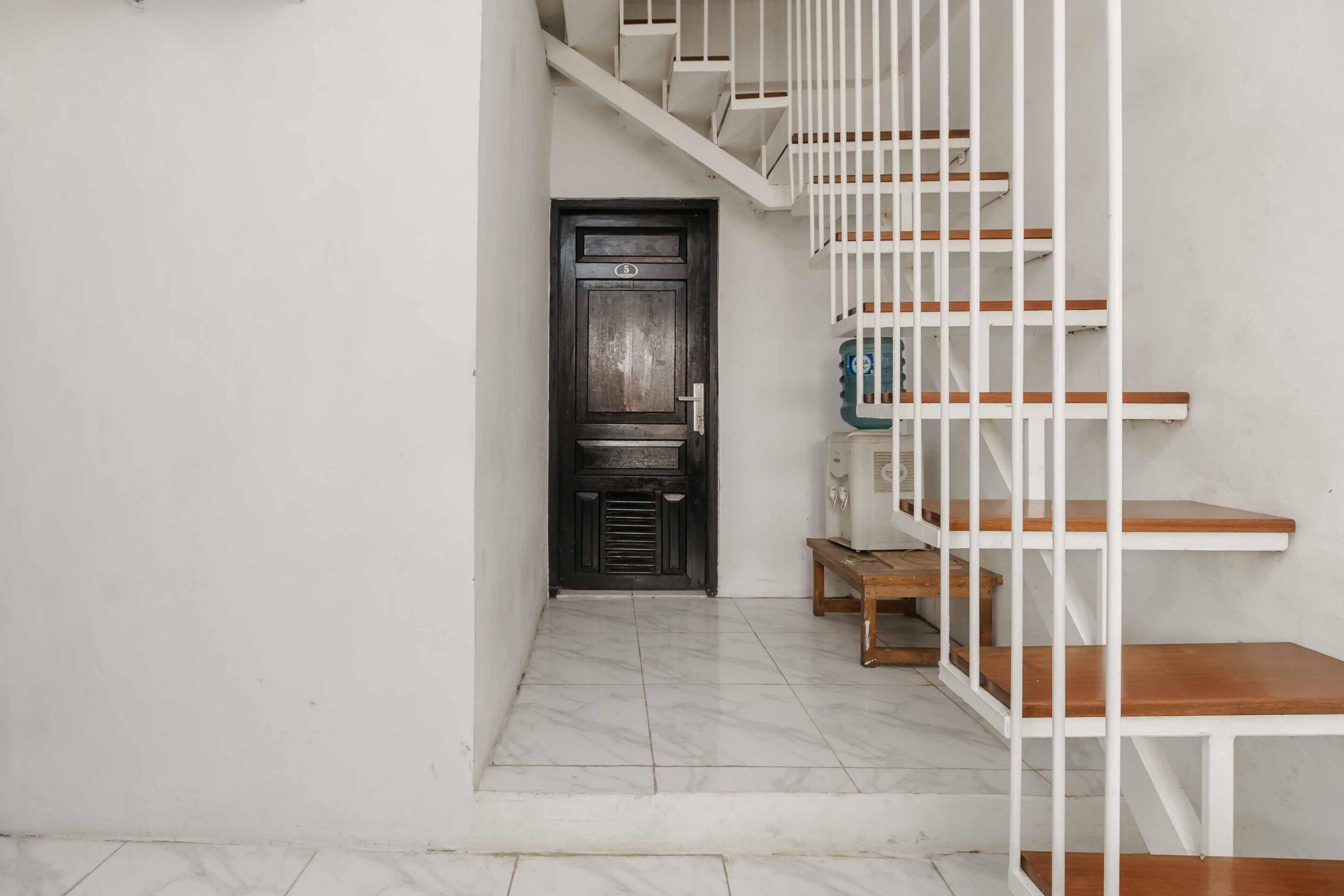 A staircase with white railings and wooden steps leading to a dark wooden door with a number plate.